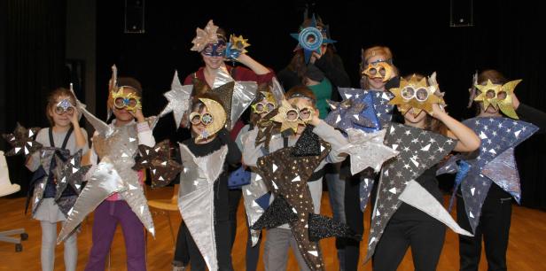 Eine Gruppe Kinder in Sternenkostümen und Masken posiert auf einer Bühne.