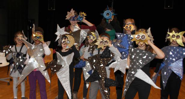 Eine Gruppe von Kindern in Sternenkostümen und Masken steht auf einer Bühne.