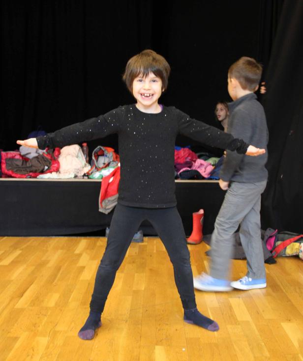 Ein lächelndes Mädchen steht mit ausgestreckten Armen auf einer Bühne.