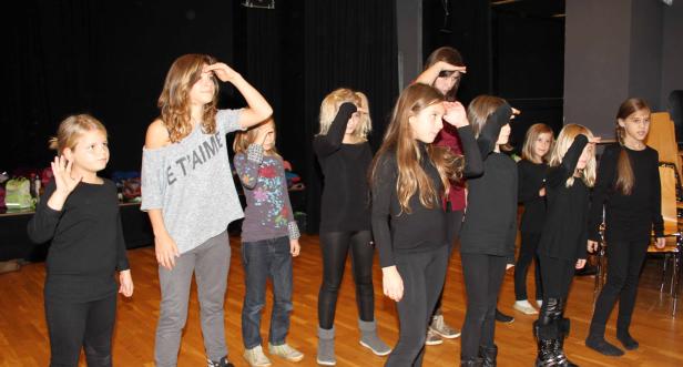 Eine Gruppe von Mädchen steht auf einer Bühne und hält die Hand an die Stirn.