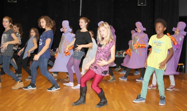 Eine Gruppe von Kindern führt ein Theaterstück auf einer Bühne auf.