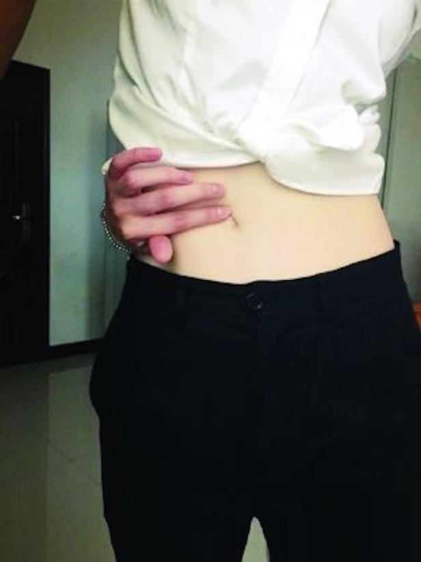 Eine Person in schwarzer Hose und weißem Hemd berührt ihren Bauchnabel.