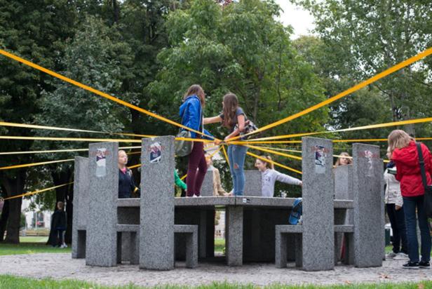Eine Gruppe von Jugendlichen steht an einem Steintisch, umgeben von gelben Bändern.