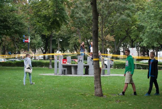 Eine Gruppe von Menschen befindet sich in einem Park mit einem ungewöhnlichen Tisch und gelbem Absperrband.