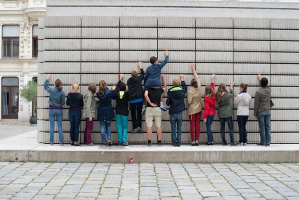 Eine Gruppe von Kindern steht vor einer Wand und versucht, diese zu erklimmen.