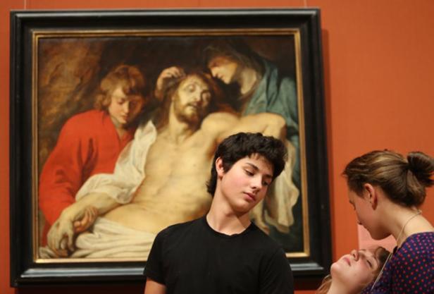 Drei junge Leute betrachten ein Gemälde, das die Grablegung Christi darstellt.