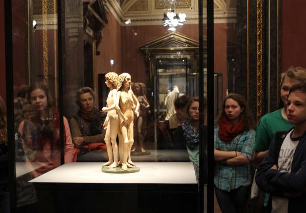 Besucher betrachten eine Skulptur von drei miteinander verbundenen weiblichen Figuren in einem Museum.
