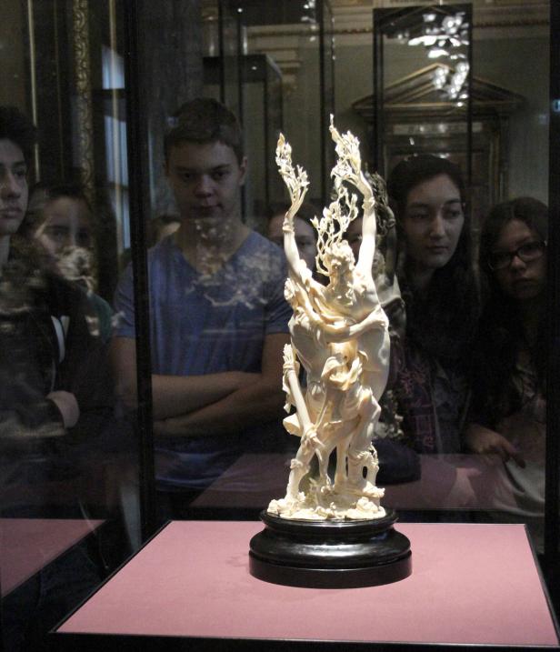 Eine Elfenbeinskulptur in einer Vitrine, betrachtet von mehreren Personen.