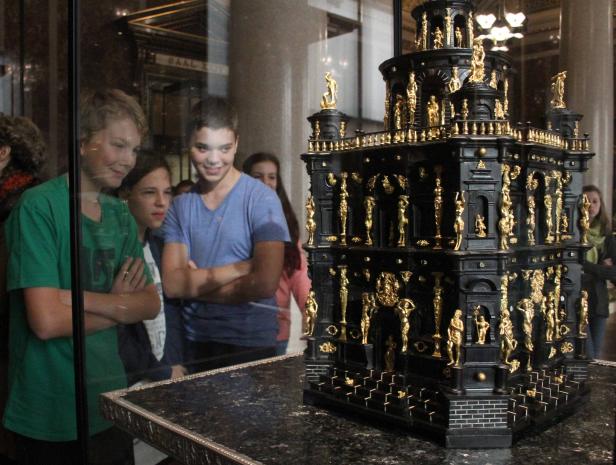 Besucher betrachten ein aufwendiges, schwarzes Modell mit goldenen Statuen in einem Museum.