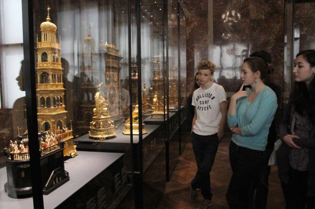 Besucher betrachten goldene Kunstobjekte in einer Vitrine.
