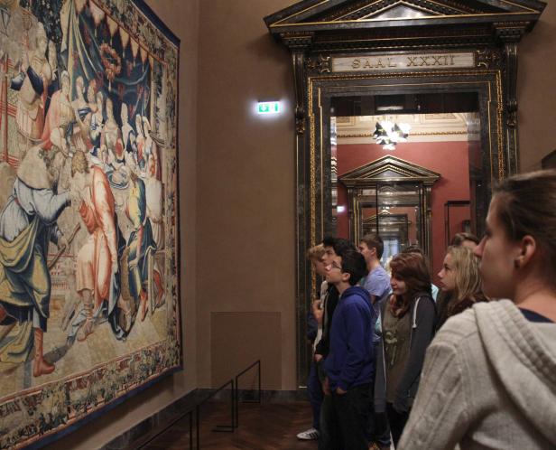 Eine Gruppe von Menschen betrachtet einen Wandteppich in Saal XXXII eines Museums.