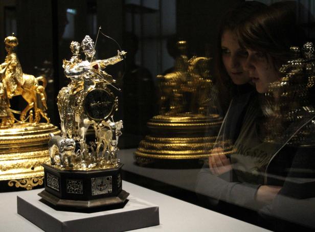 Zwei Frauen betrachten eine kunstvolle Uhr mit Figuren in einem Museum.