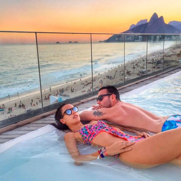 Ein Paar entspannt in einem Pool mit Blick auf den Strand von Rio de Janeiro bei Sonnenuntergang.