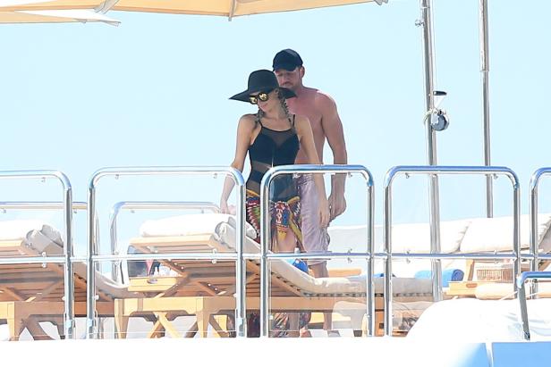Eine Frau mit Hut und ein Mann stehen auf dem Deck einer Yacht.
