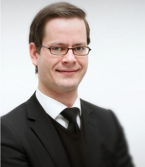 Ein Mann mit Brille, Anzug und Krawatte lächelt in die Kamera.