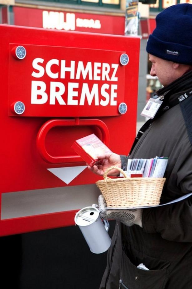 Ein Mann verteilt „Schmerzbremse“-Produkte an einem roten Stand.