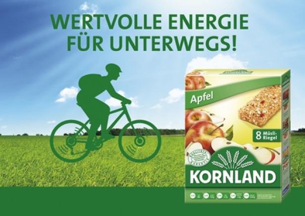 Ein Kornland Apfel Müsliriegel vor einer Landschaft mit Radfahrer.