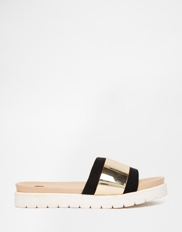 Ein goldener Pantoletten-Sandalen mit schwarzem Riemen und Plateausohle.