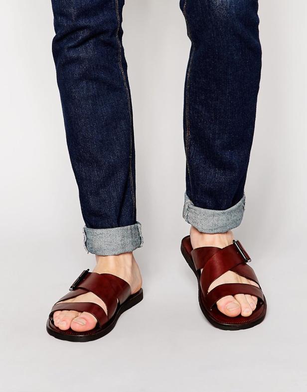 Eine Person trägt Jeans und braune Ledersandalen.