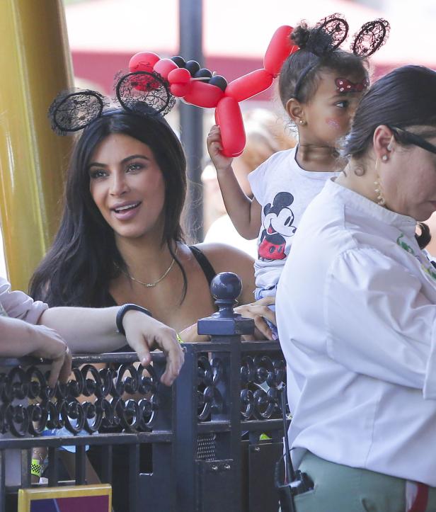 Kim Kardashian mit ihrer Tochter in einem Vergnügungspark, beide mit Mickey-Mouse-Ohren.