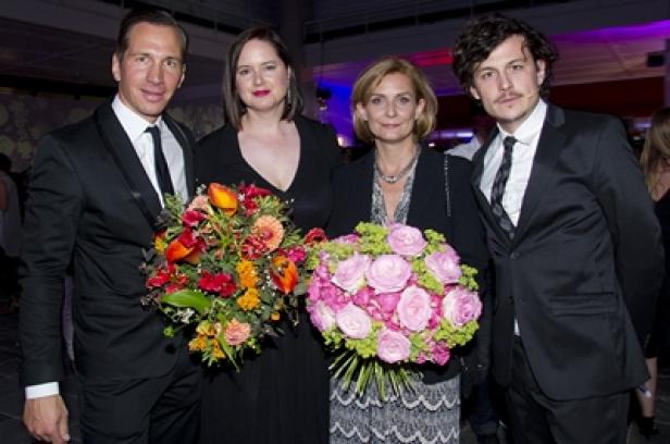 Vier Personen in Abendgarderobe posieren mit Blumensträußen für ein Foto.
