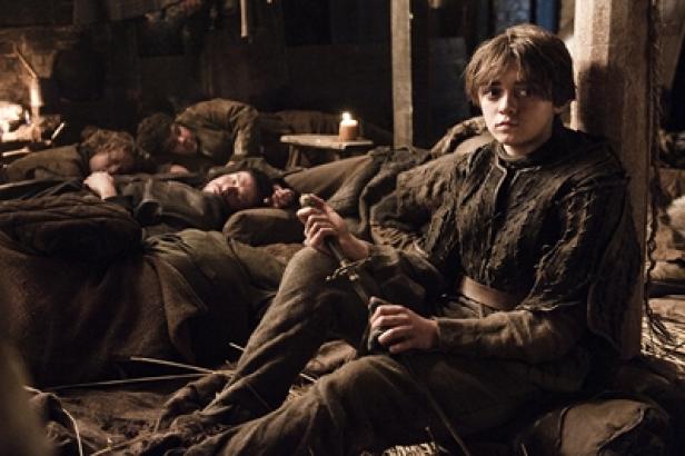 Arya Stark sitzt mit einem Schwert in einem Raum, während andere schlafen.