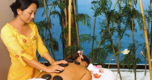 Eine Frau erhält eine Hot-Stone-Massage in einem Spa mit Blick auf das Meer.