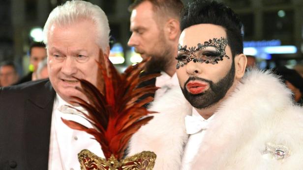 Zwei Männer, einer mit einer venezianischen Maske und einem weißen Pelzmantel, posieren für ein Foto.