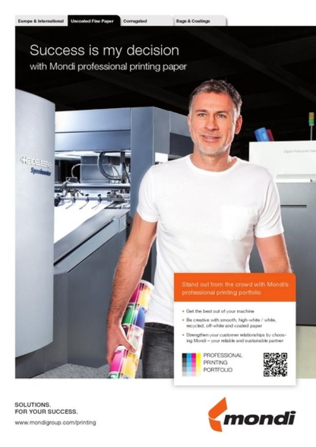 Ein Mann steht vor einer Druckmaschine und hält eine Rolle bedrucktes Papier in der Hand.
