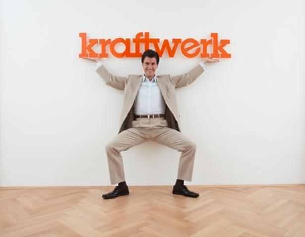 Ein Mann im Anzug stemmt den Schriftzug „Kraftwerk“ an einer Wand.