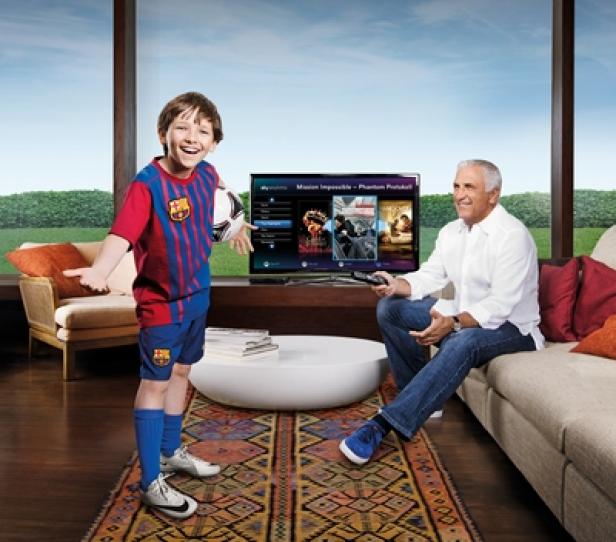 Sky-TV-Spot - Sky+ - Morgan Heath und Hans Krankl - move121 - Moving Target Films - Making of (c: sky) Ein Junge im Fußballtrikot steht mit einem Ball vor einem Fernseher, während ein Mann auf der Couch sitzt und fernsieht.