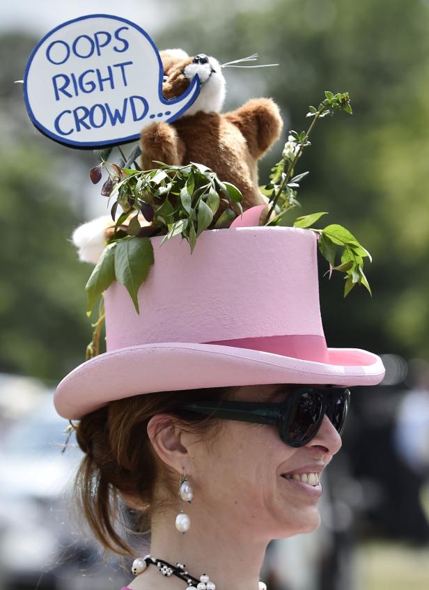 Eine Frau trägt einen extravaganten rosa Hut mit einem Stofftier und einem Schild mit der Aufschrift „Oops Right Crowd…“.