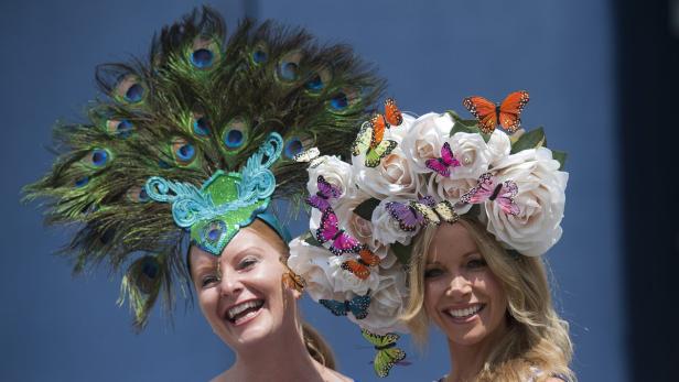 Zwei Frauen mit extravaganten Hüten, einer mit Pfauenfedern und der andere mit Rosen und Schmetterlingen.