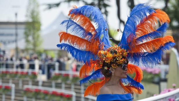 Eine Frau mit einem extravaganten Hut mit blauen und orangefarbenen Federn.