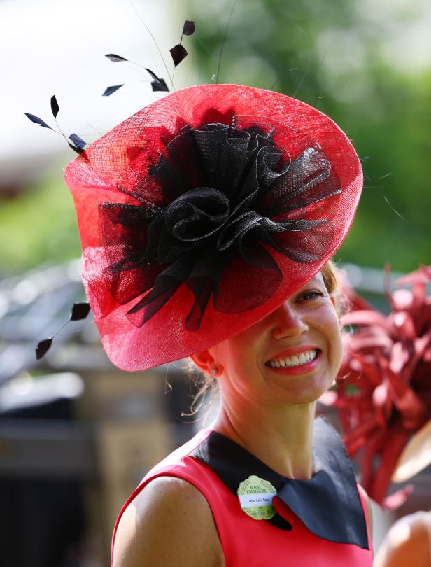 Eine Frau mit einem auffälligen roten Hut mit schwarzer Verzierung lächelt.