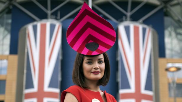 Eine Frau mit einem extravaganten Hut vor dem Hintergrund von Union-Jack-Motiven.