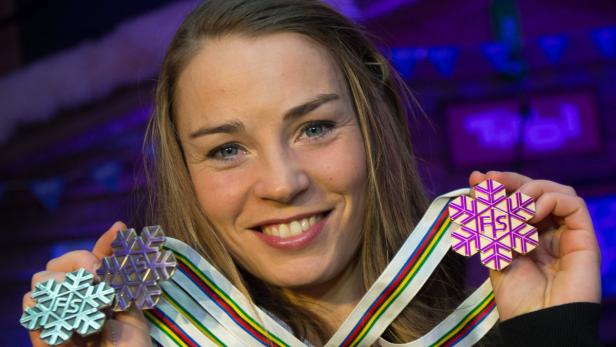 Eine Frau hält zwei Medaillen mit Schneeflocken-Design und FIS-Logo in den Händen.