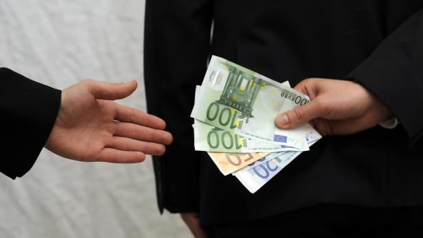 Eine Person übergibt einer anderen einen Stapel Euroscheine.