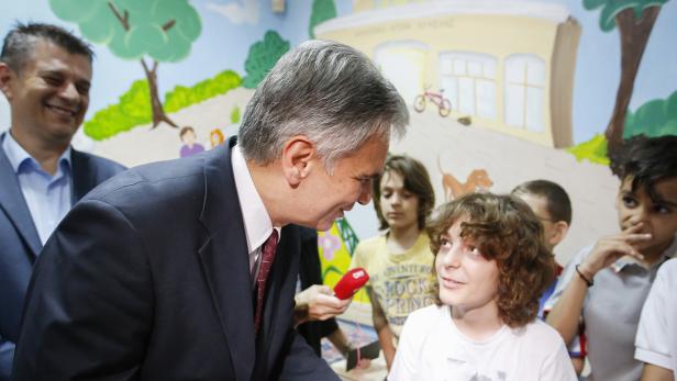 Ein Mann im Anzug spricht mit einem Jungen vor einer Wandmalerei.