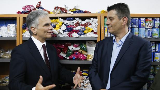 Zwei Männer in Anzügen stehen vor Regalen mit Lebensmitteln.