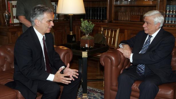 Zwei Männer in Anzügen sitzen in einem formellen Besprechungsraum und unterhalten sich.