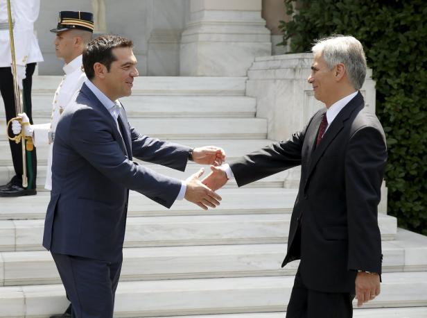 Zwei Männer in Anzügen geben sich die Hand vor einer Treppe.