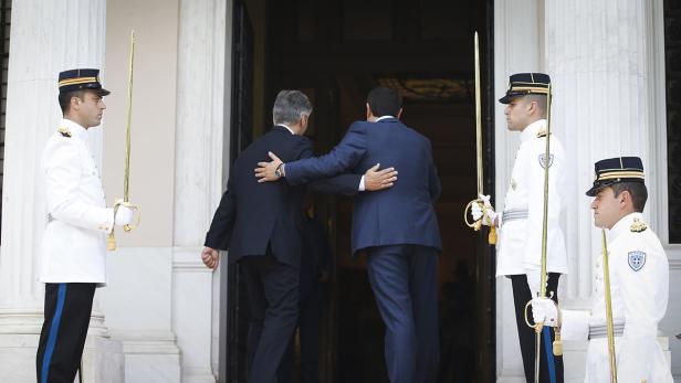Zwei Männer in Anzügen betreten ein Gebäude, flankiert von vier uniformierten Wachen mit Säbeln.