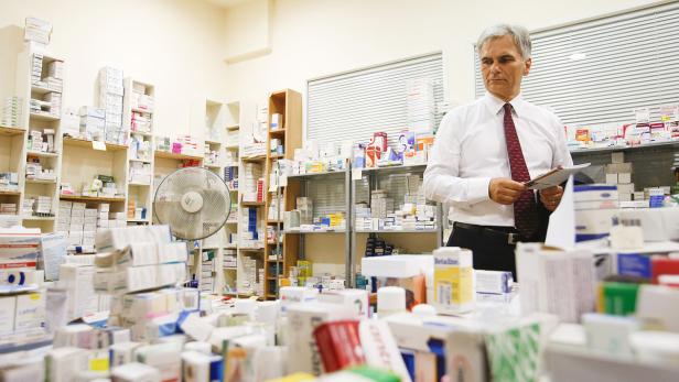 Ein Mann im weißen Hemd steht in einem Raum voller Medikamente und hält ein Dokument.