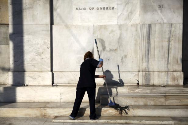 Eine Frau wischt die Stufen vor dem Gebäude der Bank von Griechenland.