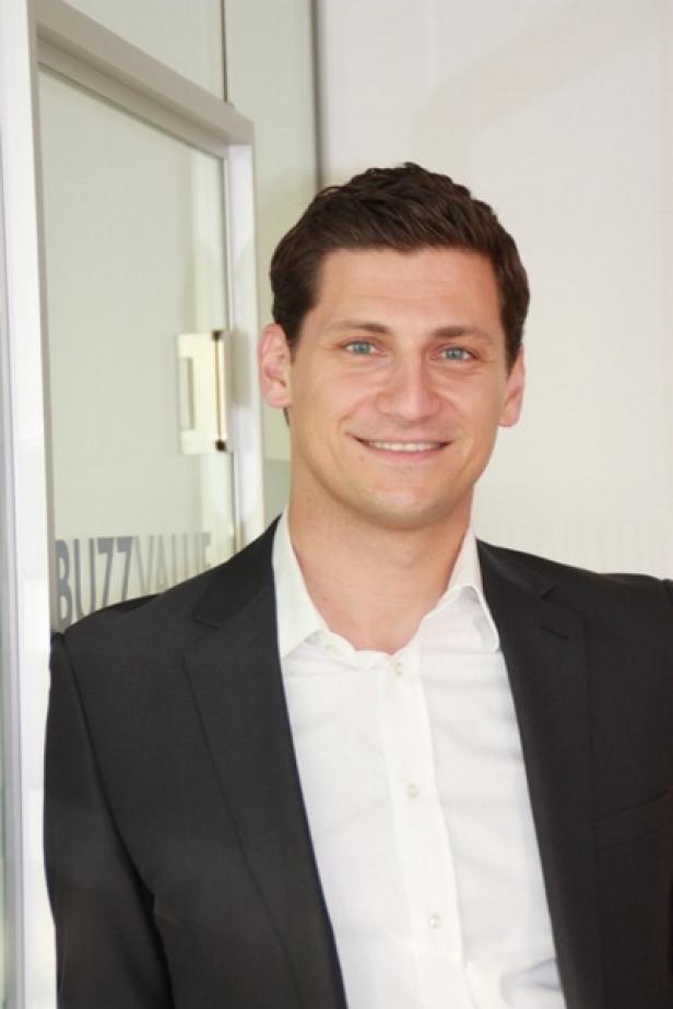 Markus Zimmer, Buzz Value und IAB Brand Buzz Driver Ein lächelnder Mann in Anzug und Hemd steht vor einer Glastür mit der Aufschrift „BuzzValue“.