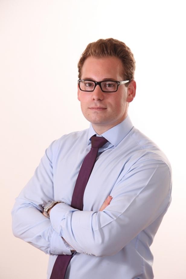 Ein Mann mit Brille, Hemd und Krawatte hat die Arme verschränkt.