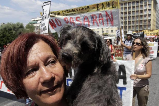Eine Frau hält einen Hund auf einer Demonstration mit Transparenten im Hintergrund.
