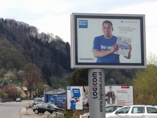 Eine Werbetafel der „Bezirksblätter“ mit einem Mann, der eine Zeitung in der Hand hält.