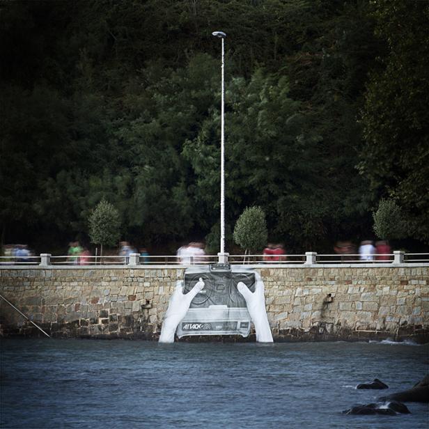 Eine Installation am Ufer zeigt Hände, die eine Fernbedienung halten, mit einem Mast, der wie eine Antenne wirkt.
